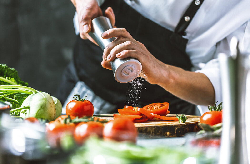 Koch würzt Tomaten mit Salzmühle