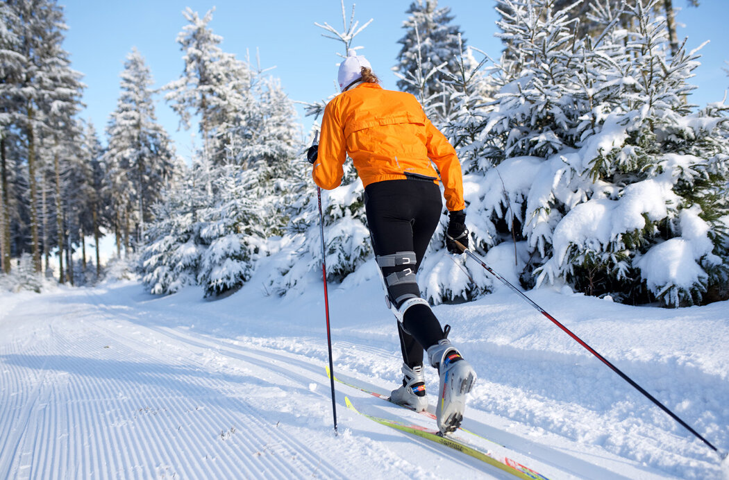Langläufer mit oranger Winterjacke von hinten auf Langlaufbahn im Winter