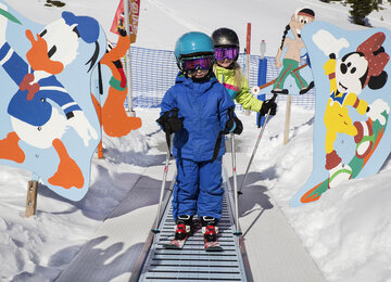 Kleiner Bub auf Skiern fährt auf Zauberteppich
