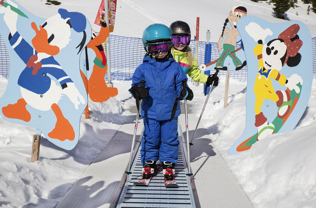 Kleiner Bub auf Skiern fährt auf Zauberteppich