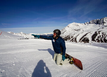 Snowboarder kniet am Boden und zeigt auf was